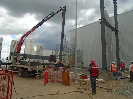 Trabajadores y grúa en sitio, montando una columna de acero estructural, parte de entender Qué es el mantenimiento industrial.