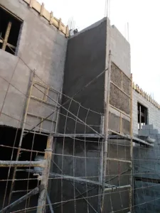 Muro en proceso de aplanado con andamios, un factor inicial para estimar Cuánto cuesta una remodelación exterior.