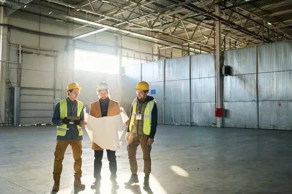 Fotografía de tres compañeros de trabajo que conocen qué es una nave industrial revisando los planos del proyecto